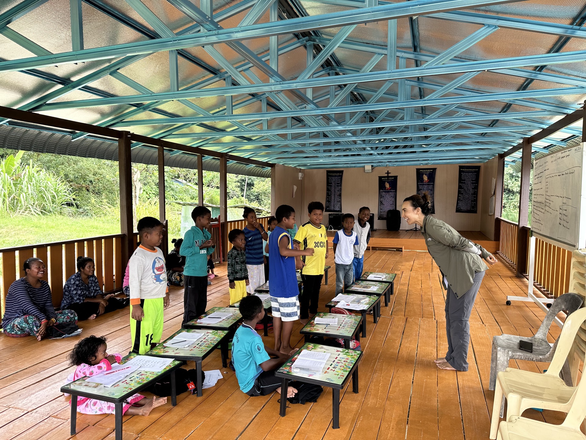 Village educator leading a group lesson for young Orang Asli learners in an outdoor community setting