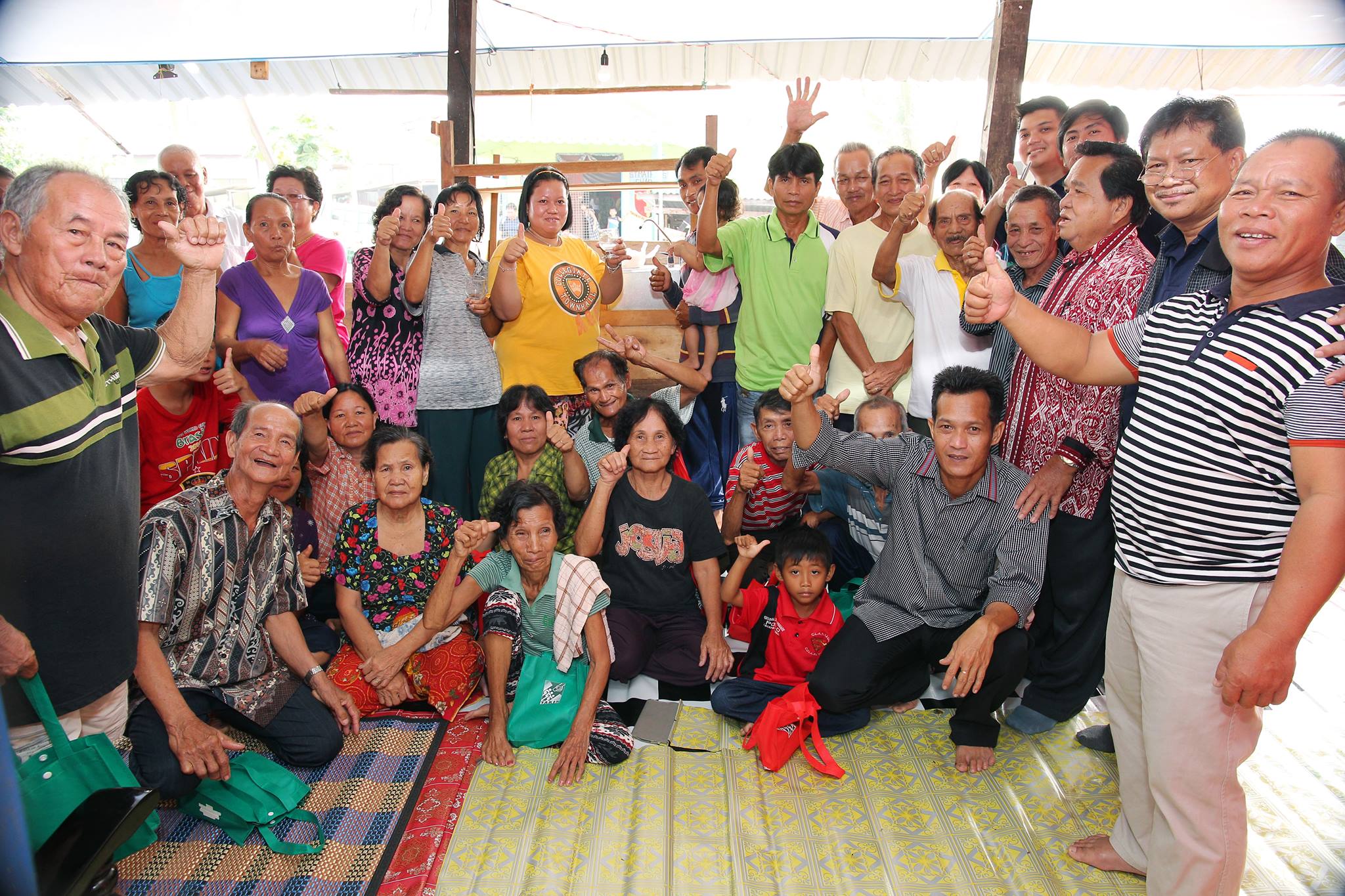 Orang Asli community members gathered together in a lush rainforest village, smiling and engaged in daily activities